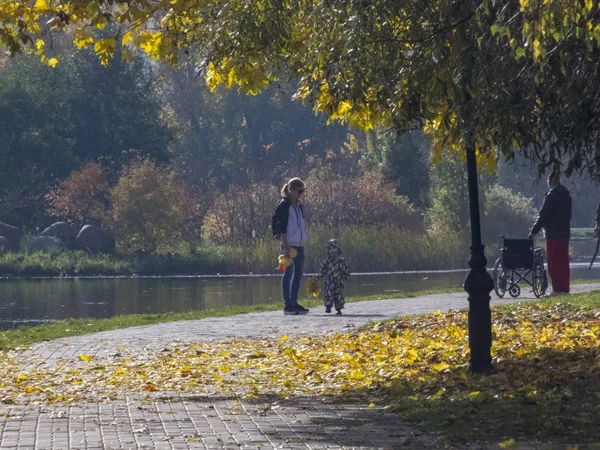 Uma mulher com um filho. Tempo de outono, outono na cidade, paisagem urbana de outono com um lago, pessoas andando e outros divertimentos — Fotografia de Stock