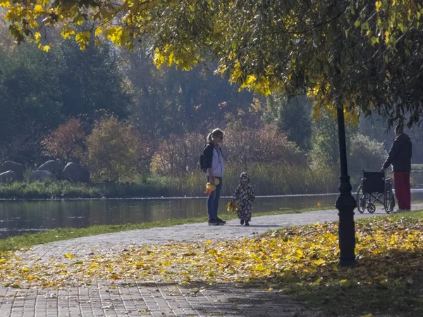 Femme avec un enfant. Automne, automne dans la ville, paysage d'automne urbain avec un étang, les gens qui marchent et d'autres amusements — Photo