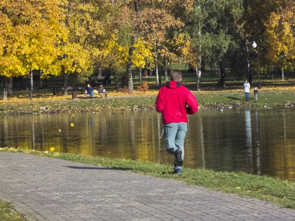 Le gars court dans le parc avec un étang à l'automne. C'est l'automne. — Photo