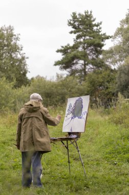 Yaşlı bir adam yağlı boya resimlerle ilgilenir.