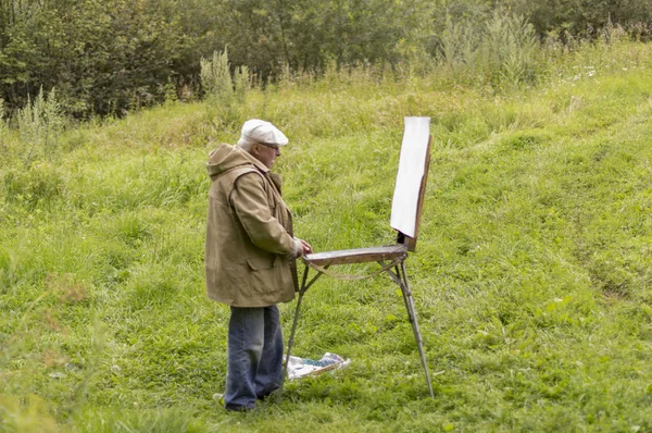 Yaşlı bir adam yağlı boya resimlerle ilgilenir.