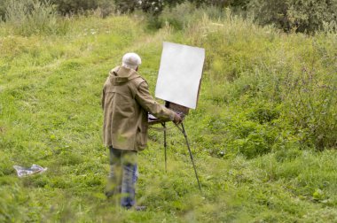 Yaşlı bir adam yağlı boyalarla resim yapmak istiyor. Doğal bir manzara çizimi