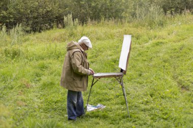 Yaşlı bir adam yağlı boyalarla resim yapmak istiyor. Doğal bir manzara çizimi