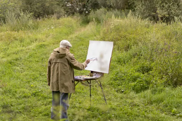 Yaşlı bir adam yağlı boyalarla resim yapmak istiyor. Doğal bir manzara çizimi Stok Fotoğraf