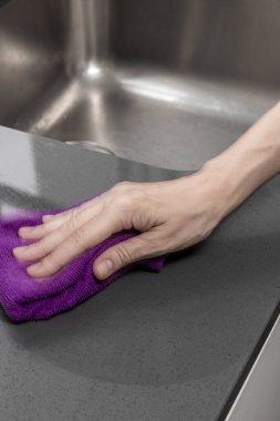 Mutfak tezgahını paslanmaz çelik lavabonun yanında mor bir bezle temizler.