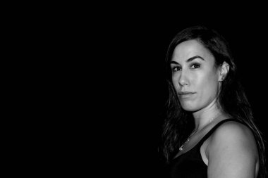 Ciddi bir ifadeyle ve uzun siyah saçlarıyla doğrudan kameraya bakan bir kadın.