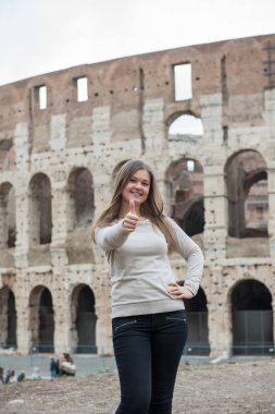 Colosseum önünde beyaz kazak giyen kız gülümseyerek, Roma, İtalya, başparmak havaya