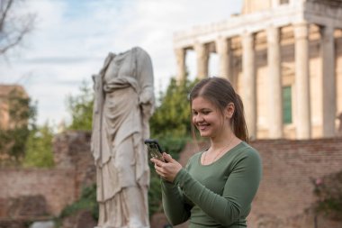 Foro Romano, Rom, İtalya, manifatura Smartphone antika Romen heykel önünde yeşil kazak giyen genç kadın