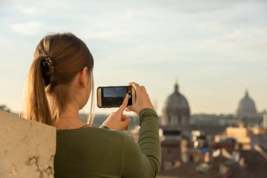 St. Peters Katedrali, Vatikan, Roma, İtalya, önünde çatıda yeşil kazak giyen genç kadın fotoğrafları onun smartphone ile alır.