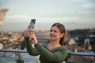 Kolezyum, Roma, İtalya, önünde çatıda yeşil kazak giyen genç kadın onun smartphone ile selfie yapar