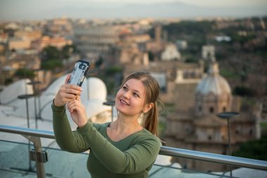 Kolezyum, Roma, İtalya, önünde çatıda yeşil kazak giyen genç kadın onun smartphone ile selfie yapar