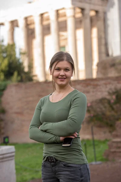 フォロ ロマーノ Rom イタリア 保持しているスマート フォンのアンティーク ルーマニア語建物の前に緑のプルオーバーを着ている若い女性 — ストック写真
