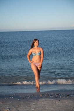 Genç bir kadın sahilde poz veriyor.