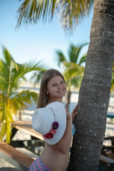 Jonge vrouw poseren tegen zee bedide palmboom met hoed — Stockfoto