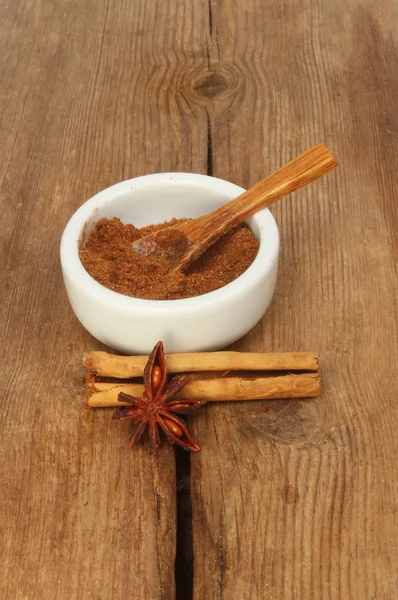 Chinese five spice in a ramekin with cinnamon and star anise on old weathered wood