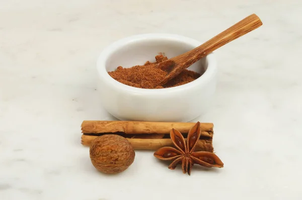 Chinese five spice in a ramekin with nutmeg, star anise and cinnamon on a marble worktop