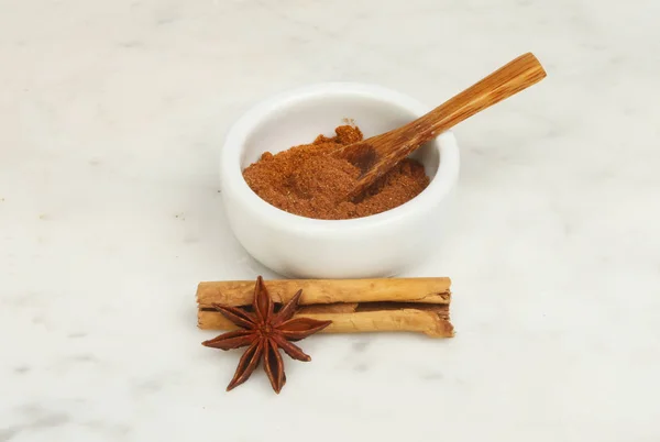 Chinese five spice in a ramekin with cinnamon and star anise on a marble worktop