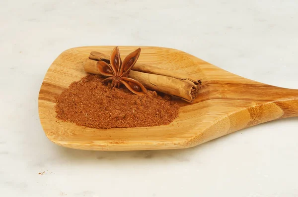 Chinese five spice, cinnamon and star anise in a wooden spoon on a marble worktop