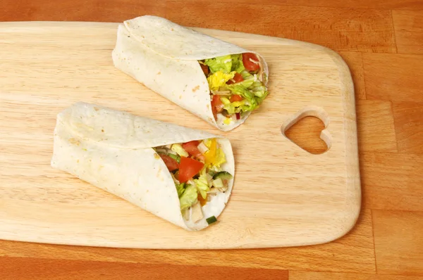 Chicken and sald sandwich wraps on a wooden chopping board with a heart shaped cutout