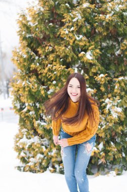 Genç koyu saçlı güzel gülümseyen kadın sarı örme kazak ve kot karda portresi Bahçe arka plan kapsamında. Karlı kış manzarası