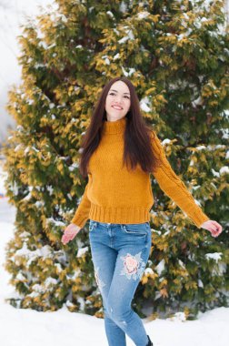 Genç koyu saçlı güzel gülümseyen kadın sarı örme kazak ve kot karda portresi Bahçe arka plan kapsamında. Karlı kış manzarası