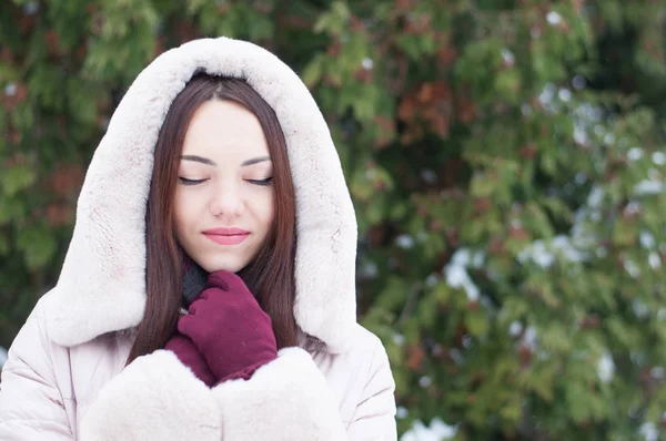 年轻美丽的情感的妇女的肖像在白雪覆盖的花园背景上头戴头套的外套和手套 冬季雪景 — 图库照片