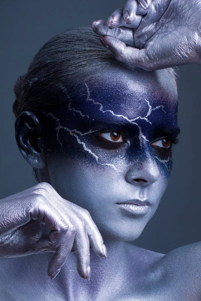 young woman with lightning face art on black background. Female lightning design body art. Blue silver face art.