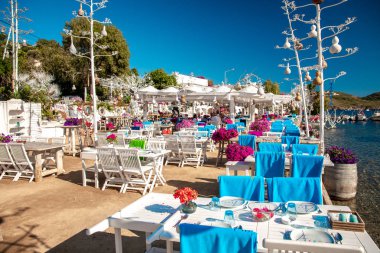 Türkiye'nin Bodrum kenti Gumusluk'ta balık restoranı, kafe ve begonviller çiçeklerinin görünümü. Ege sahil tarzı renkli sandalye ve masalar.