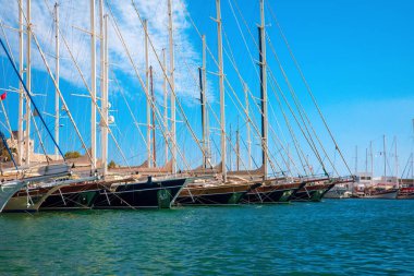 Türkiye'nin Bodrum kenti Gumusluk'ta Bodrum sahilinde balık restoranı veya kafe ve begonviller çiçeği manzarası. Güzel Ege Denizi'ne yakın Bodrum ilçesinde Ege sahil tarzı renkli sandalyeler, evler, marina, yelkenli tekneler, yatlar, masalar ve çiçekler.