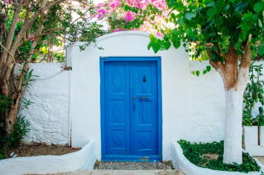 Türkiye'nin Bodrum kenti Gumusluk'ta Bodrum sahilinde balık restoranı veya kafe ve begonviller çiçeği manzarası. Güzel Ege Denizi'ne yakın Bodrum ilçesinde Ege sahil tarzı renkli sandalyeler, evler, marina, yelkenli tekneler, yatlar, masalar ve çiçekler.