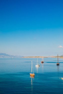 Türkiye'nin Bodrum kenti Gumusluk'ta Bodrum sahilinde balık restoranı veya kafe ve begonviller çiçeği manzarası. Güzel Ege Denizi'ne yakın Bodrum ilçesinde Ege sahil tarzı renkli sandalyeler, evler, marina, yelkenli tekneler, yatlar, masalar ve çiçekler.