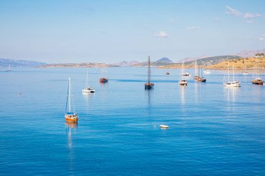 Türkiye'nin Bodrum kenti Gumusluk'ta Bodrum sahilinde balık restoranı veya kafe ve begonviller çiçeği manzarası. Güzel Ege Denizi'ne yakın Bodrum ilçesinde Ege sahil tarzı renkli sandalyeler, evler, marina, yelkenli tekneler, yatlar, masalar ve çiçekler.