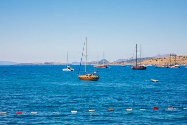 Türkiye'nin Bodrum kenti Gumusluk'ta Bodrum sahilinde balık restoranı veya kafe ve begonviller çiçeği manzarası. Güzel Ege Denizi'ne yakın Bodrum ilçesinde Ege sahil tarzı renkli sandalyeler, evler, marina, yelkenli tekneler, yatlar, masalar ve çiçekler.