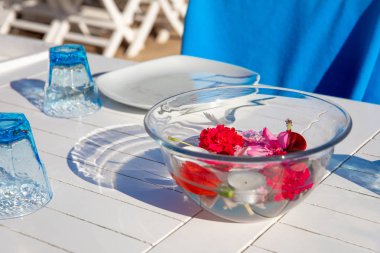 Türkiye'nin Bodrum kenti Gumusluk'ta Bodrum sahilinde balık restoranı veya kafe ve begonviller çiçeği manzarası. Güzel Ege Denizi'ne yakın Bodrum ilçesinde Ege sahil tarzı renkli sandalyeler, evler, marina, yelkenli tekneler, yatlar, masalar ve çiçekler.