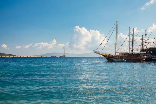 Türkiye'nin Bodrum kenti Gumusluk'ta Bodrum sahilinde balık restoranı veya kafe ve begonviller çiçeği manzarası. Güzel Ege Denizi'ne yakın Bodrum ilçesinde Ege sahil tarzı renkli sandalyeler, evler, marina, yelkenli tekneler, yatlar, masalar ve çiçekler.