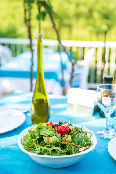Greek, Mediterranean or Aegean Green fresh vegetarian Salad on the table in Fish Restaurant. Green Salad in bowl with olive oil at Beach Fish Restaurant in Greece or Turkey.