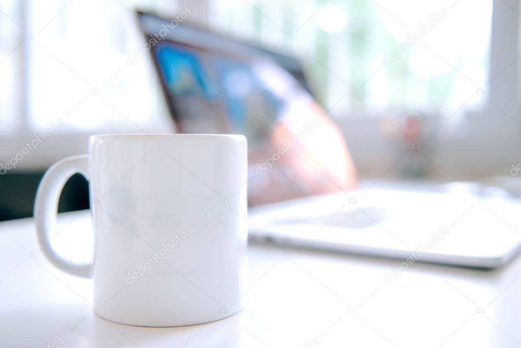 Coffee mug or cup and laptop on the table in office interior. Bussiness and technology concept image.