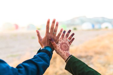 Genç ve mutlu bir çift el ele tutuşuyor. Erkek ya da erkek ve kız ellerini tutuyorlar. Kızın hanı kınalı. Asyalı çift birbirini seviyor.