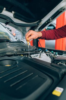 Motor bakımı sırasında garajda çalışan oto tamircisi. Oto servis garajında bir araba tamiri sırasında tamirci itme dipstick