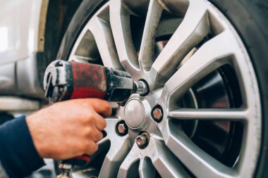 Oto tamirhanesinde tamirci değişen araba tekerleği. Tamirci tamir aracı garajında el ve alet kullanarak lastik tekerleği ayarlama