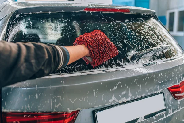 Car wash and detailing - the man holds the microfiber in hand and polishes or washing the car. Man cleaning automobile with sponge at car wash