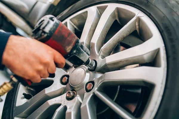 Oto tamirhanesinde tamirci değişen araba tekerleği. Tamirci tamir aracı garajında el ve alet kullanarak lastik tekerleği ayarlama