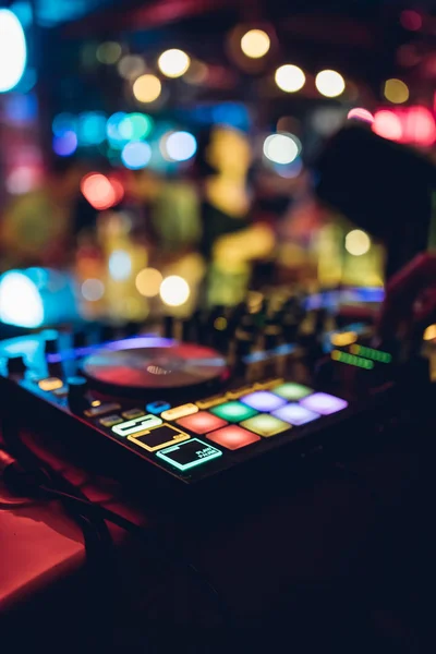 DJ plays live set and mixing music on turntable console at stage in the night club. Disc Jokey Hands on a sound mixer station at club party. DJ mixer controller panel for playing music and partying.