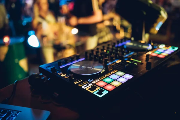 DJ plays live set and mixing music on turntable console at stage in the night club. Disc Jokey Hands on a sound mixer station at club party. DJ mixer controller panel for playing music and partying.