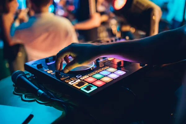 DJ plays live set and mixing music on turntable console at stage in the night club. Disc Jokey Hands on a sound mixer station at club party. DJ mixer controller panel for playing music and partying.