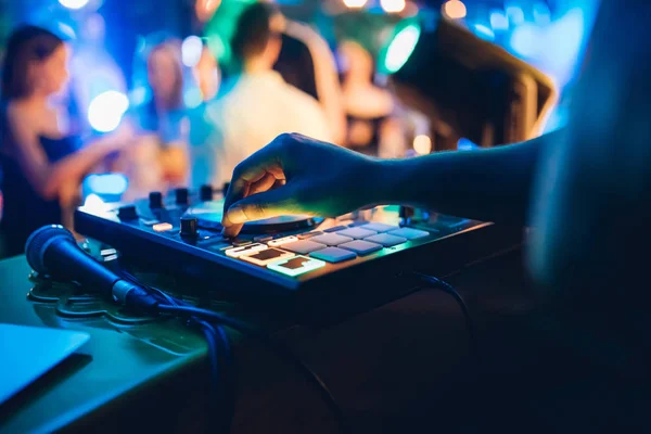 DJ plays live set and mixing music on turntable console at stage in the night club. Disc Jokey Hands on a sound mixer station at club party. DJ mixer controller panel for playing music and partying.