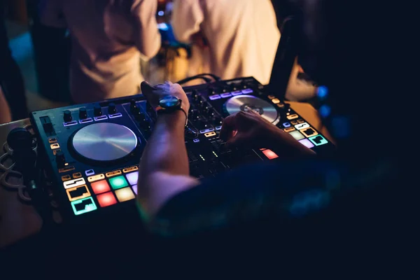 DJ plays live set and mixing music on turntable console at stage in the night club. Disc Jokey Hands on a sound mixer station at club party. DJ mixer controller panel for playing music and partying.