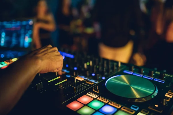 DJ plays live set and mixing music on turntable console at stage in the night club. Disc Jokey Hands on a sound mixer station at club party. DJ mixer controller panel for playing music and partying.