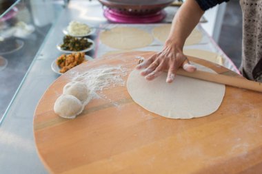 Kadın hazırlama veya borek veya ekmek hamuru yapma. Eller un ile hamur üzerinde oklava tutmak. Borek, ekmek veya ahşap bir masa arka plan üzerinde hamur pasta. Geleneksel Türk pide, pide veya yufka ekmeği.