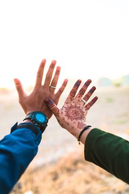 Genç ve mutlu bir çift el ele tutuşuyor. Erkek ya da erkek ve kız ellerini tutuyorlar. Kızın hanı kınalı. Asyalı çift birbirini seviyor.